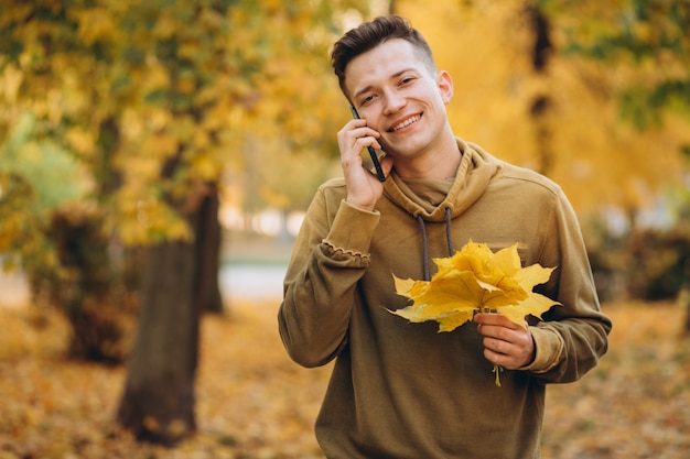 Portrait of handsome and happy guy smiling and talking on the phone in the autumn park