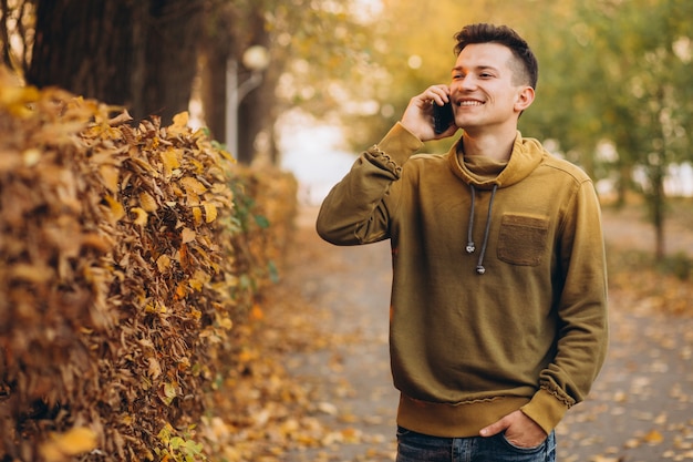 Portrait of handsome and happy guy smiling and talking on the phone in the autumn park