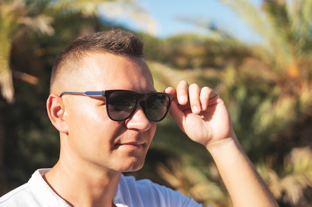 Portrait of handsome happy man in white shirt on a palm beach.