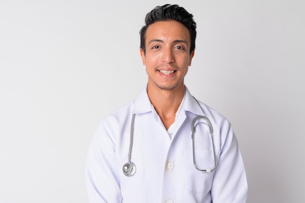 Portrait of handsome Hispanic man doctor against white wall