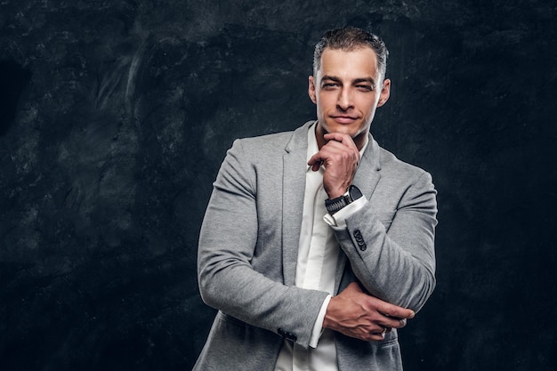 Portrait of handsome intellegent man in suit and white shirt at dark photo studio.