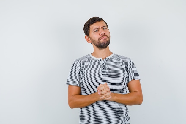 Portrait of handsome man keeping fingers clasped in t-shirt and looking thoughtful front view