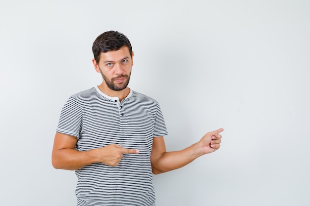 Portrait of handsome man pointing to the right side in t-shirt and looking confident front view