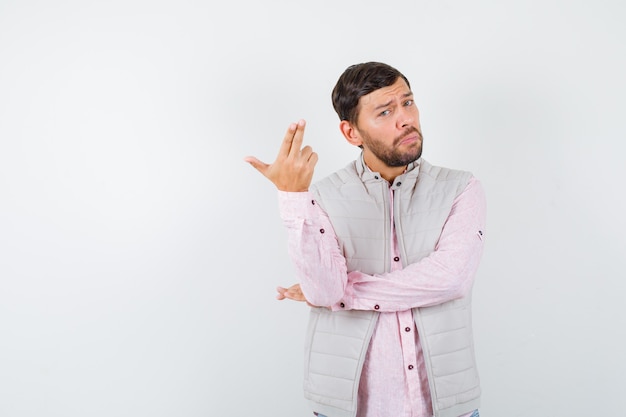 Portrait of handsome man showing gun gesture in vest, shirt and looking confident 