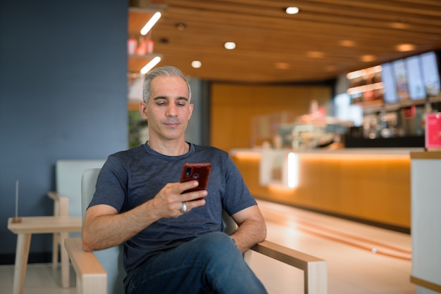 Portrait of handsome man sitting at coffee shop using mobile phone horizontal shot