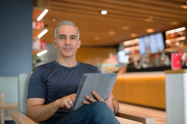 Portrait of handsome man sitting at coffee shop while holding digital tablet and looking at camera horizontal shot with copy space