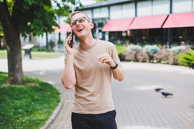 Portrait of handsome mature businessman holding messenger bag wearing stylish eyeglasses looking at camera Smiling middle aged man using smartphone standing on the street Mobile banking concept