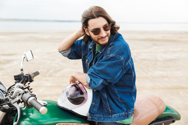 Portrait of a handsome positive optimistic happy man biker on his bike outdoors on a beach.