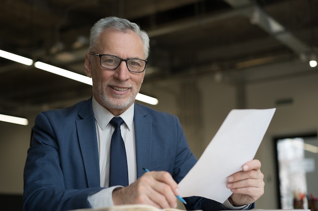 Portrait of handsome senior businessman holding documents working in office