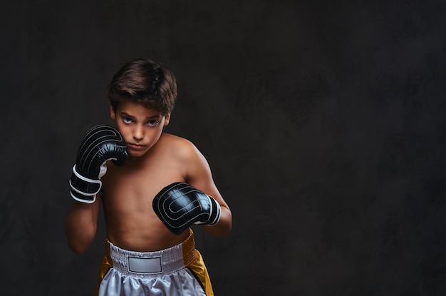 Portrait of a handsome shirtless young boxer wearing gloves, looking at a camera. Isolated on the dark background.