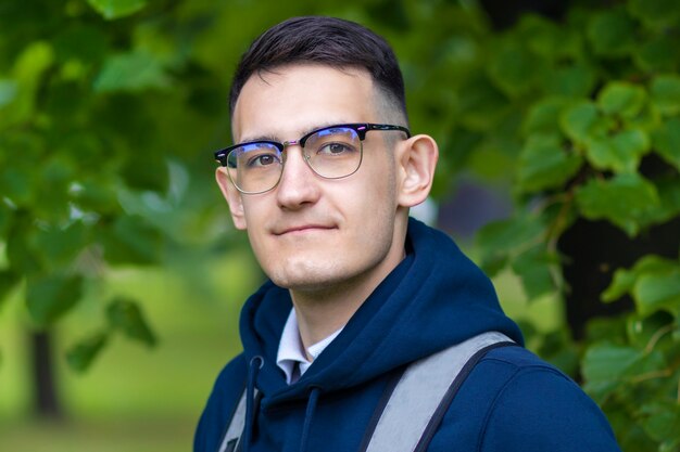 portrait of handsome smart college student outdoors in green park