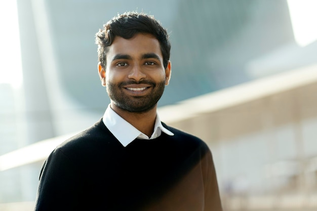 Portrait of handsome smiling Indian man looking at camera standing on the street