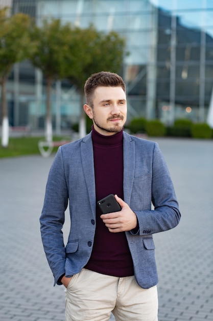 Portrait of handsome smiling man in casual wear holding smartphone