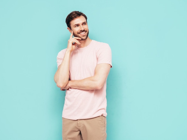 Portrait of handsome smiling stylish hipster lambersexual model Sexy man dressed in pink Tshirt and trousers Fashion male isolated on blue wall in studio