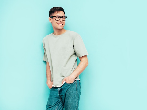 Portrait of handsome smiling stylish hipster lambersexual modelMan dressed in Tshirt and jeans Fashion male isolated in studio Posing near blue wall Cheerful and happy