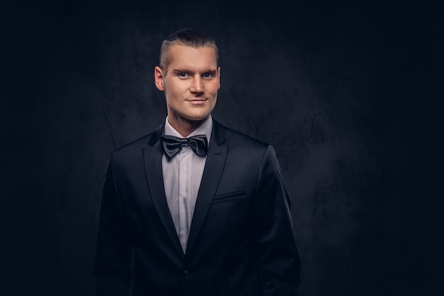 Portrait of a handsome stylish man in an elegant black suit over a dark background.