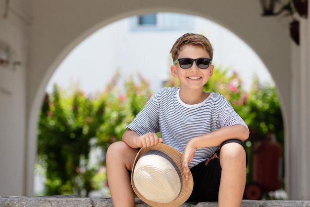 Portrait of handsome summer kid at sunny day Happy smiling schoolboy in striped tshirt and sunglasses posing outdoor lookind to camera