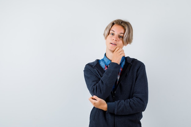 Portrait of handsome teen boy touching his chin in shirt, hoodie and looking hopeful front view