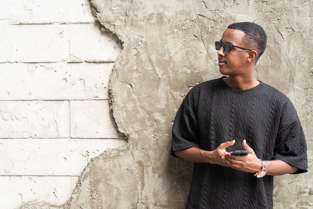 Portrait of handsome young African man using mobile phone outdoors