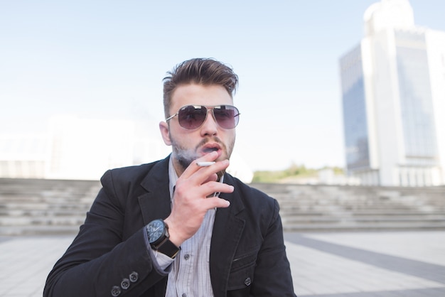 Portrait of a handsome young businessman smiling a cigarette on a city