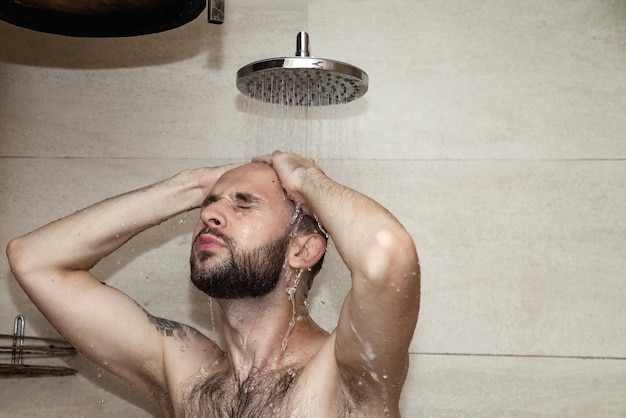 Portrait handsome young guy taking shower washing standing under falling water in bathhouse