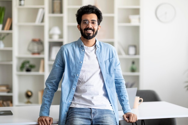 Portrait of handsome young indian man standing near desk at home