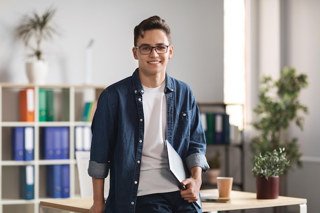 Portrait Of Handsome Young Male Entrepreneur Holding Laptop And Posing In Office