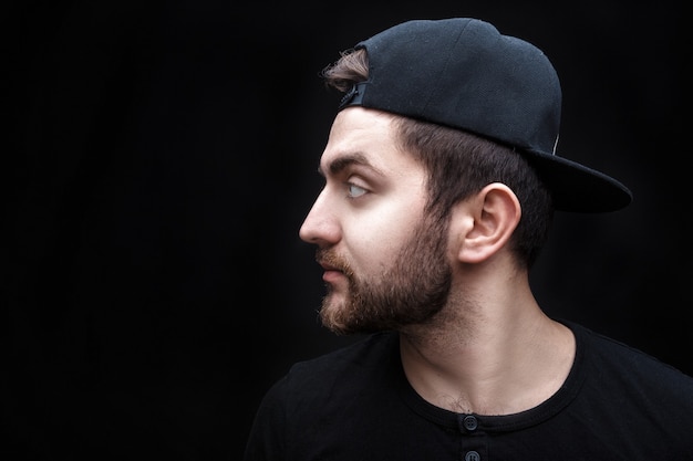 Portrait of handsome young man in black shirt and cap on black background rapper