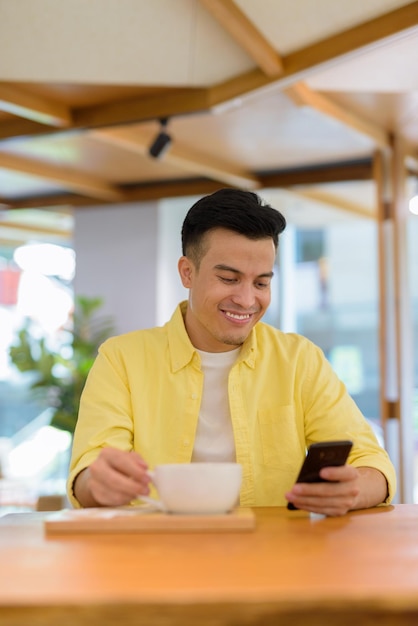 Portrait of handsome young man at coffee shop smiling and using mobile phone