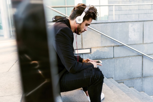 Portrait of handsome young man listening to music with mobile phone in the street.