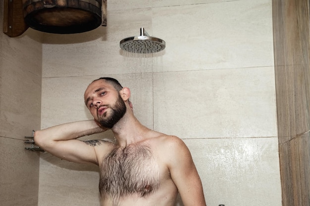 Portrait handsome young man taking shower washing standing under falling water in bathhouse