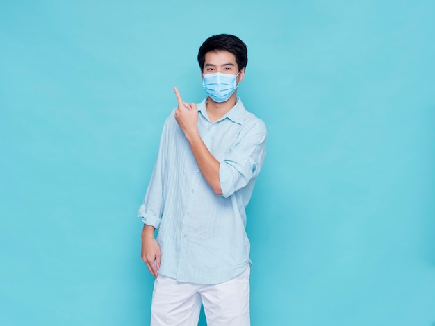 Portrait of handsome young man wearing medical mask in casual clothes pointing finger up. concept covid 19