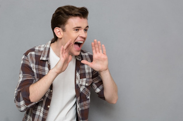 Portrait of handsome young  screaming man in plaid shirt isolated on gray wall