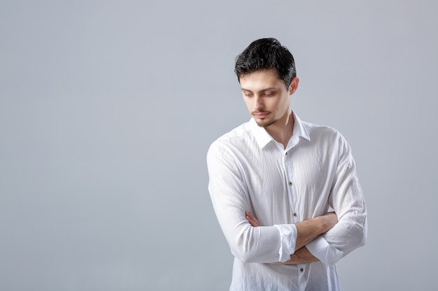 Portrait of handsome young serious man with dark hair in white shirt on gray background