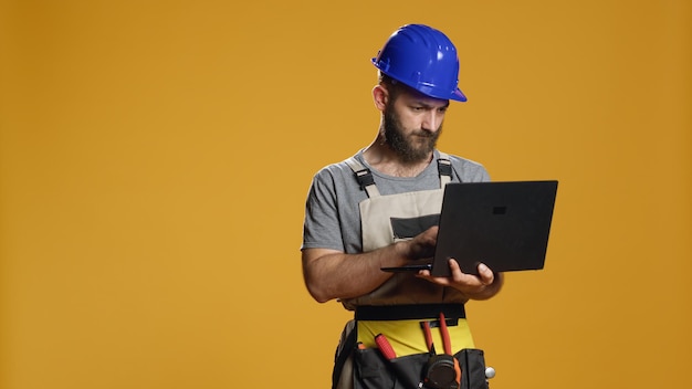 Portrait of handyman using laptop to find construction inspiration and work on refurbishment scheme or plan. Browsing internet on pc to do measurement and engineering process in studio.