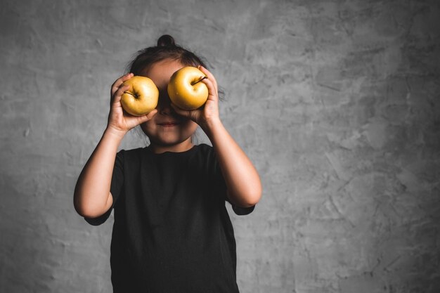 Photo portrait of a happiness little girl eating a green apple on gray background. health, wholesome food