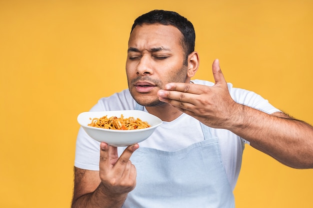 Portrait of of happy african american indian black man chef cooking pasta. Cooking, profession, haute cuisine, food and people concept isolated over yellow background.