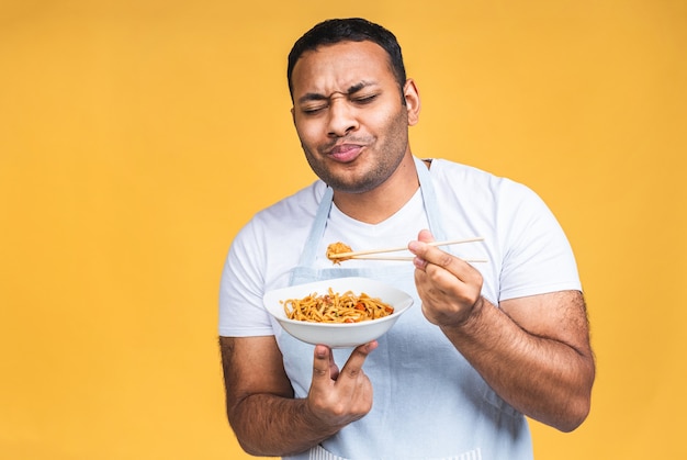 Portrait of of happy african american indian black man chef cooking pasta. Cooking, profession, haute cuisine, food and people concept isolated over yellow background.