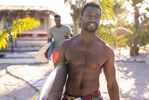 Portrait of happy african american man holding surfboard and smiling at beach. Spending quality time, lifestyle, summertime and vacation concept.