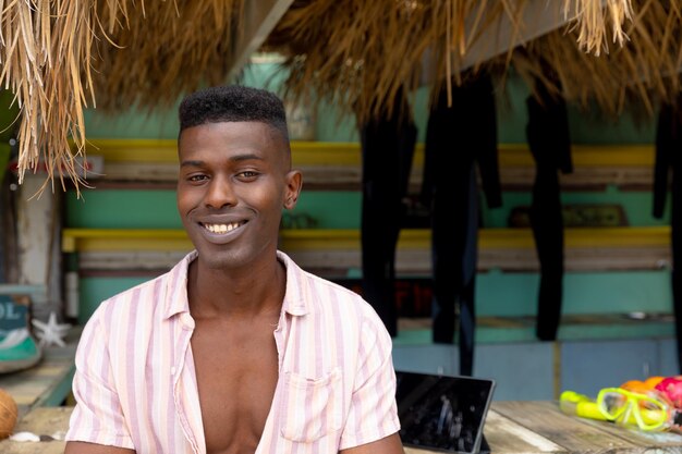 Portrait of happy african american man leaning on counter of surf hire beach shack, copy space. Local business, hobbies, sport, surfing, summer and vacation, unaltered.