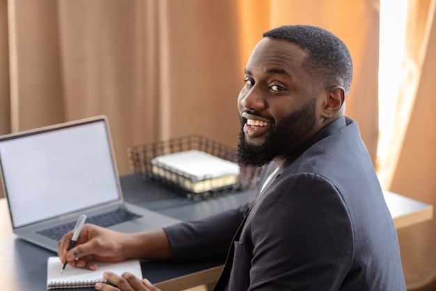 Portrait of happy African American successful businessman looks at the camera and smiling sitting in the office at the table