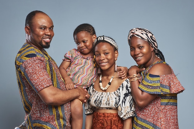 Portrait of happy african family of four in national clothing embracing and smiling at camera standi