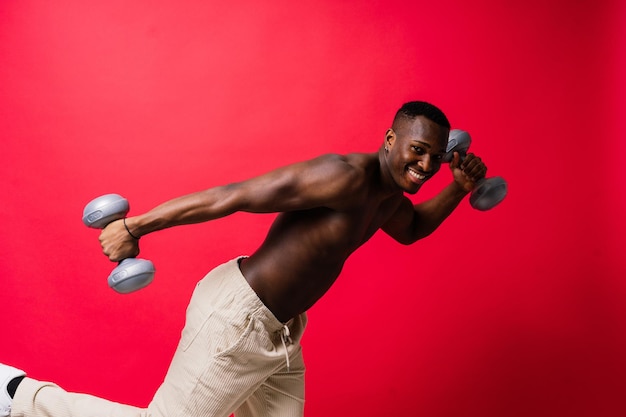 Portrait of a happy african man with dumbbells over red background