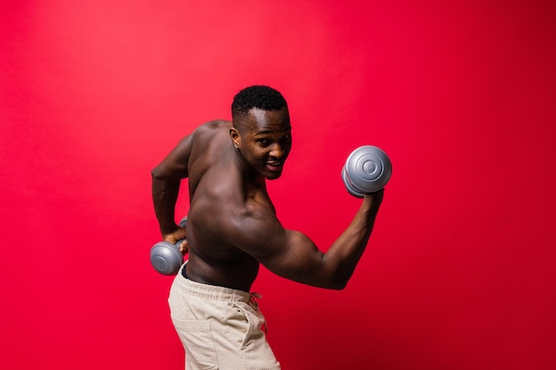 Portrait of a happy african man with dumbbells over red background