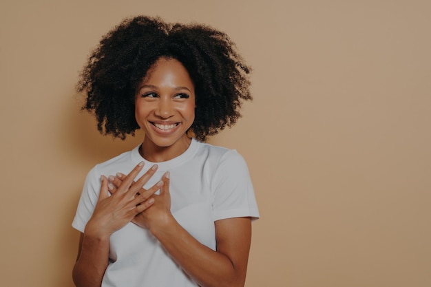 Portrait of happy african woman posing with smile looking away holding hands on chest