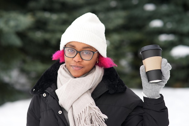 Portrait of happy afro american young woman at winter snowy day in snow park smile drink coffee