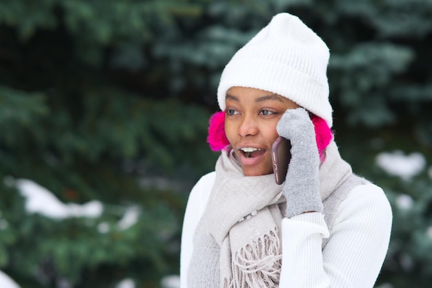 Portrait of happy afro american young woman at winter snowy day use phone in snow park smile