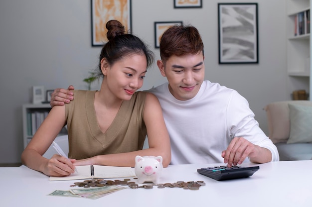 Portrait of a happy Asian couple at home saving money in a piggybank Happy woman and man couple at home saving money in a piggybank and smiling