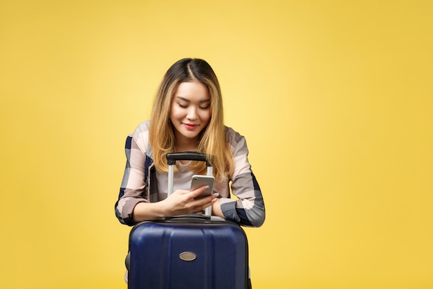 Photo portrait of happy asian female traveler with suitcase and looking at cellphone