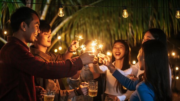 Portrait of Happy Asian group of friends having fun with sparklers outdoor Young people having fun with fireworks at night time People food drink lifestyle new year celebration concept